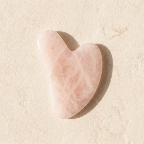 Gua sha de cuarzo rosa sobre superficie crema